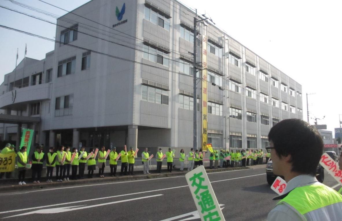 交通安全のプラカードを持ち、蛍光色のベストを身に着け街頭に並ぶ大勢の関係者らの写真