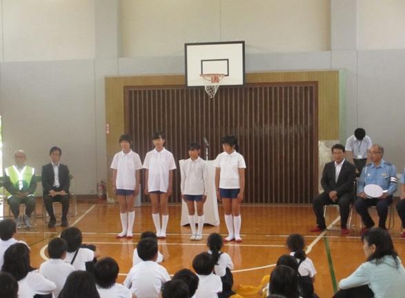 自転車大会参加者4名の選手が児童らの前に並んで立っている写真