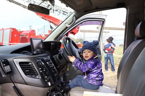 車両の運転席に座りハンドルを握る幼児の写真