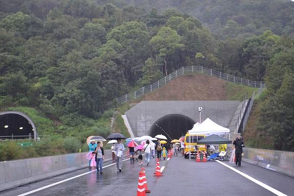 高松自動車道4車線化記念イベントに傘を差し来場する一般客らの写真