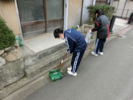 民家の前の通りを清掃する中学生らの写真