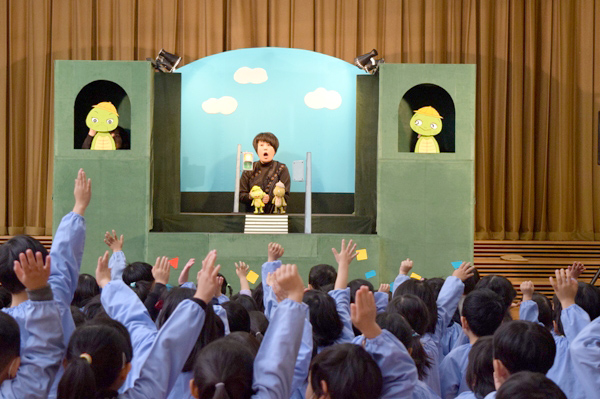 交通安全人形劇を見ながら元気に手を挙げる園児らの写真