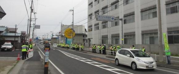 交通安全キャンペーンのため蛍光色のベストを身に関係者らが道路沿いで立哨している様子の写真