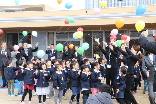 園庭で記念の風船を飛ばす園児らの様子の写真