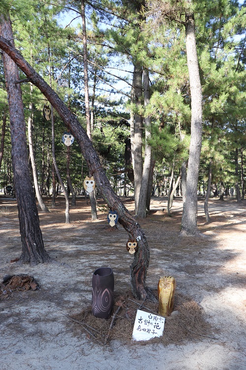 たくさんのふくろうのイラスが木につけられている造形物の写真