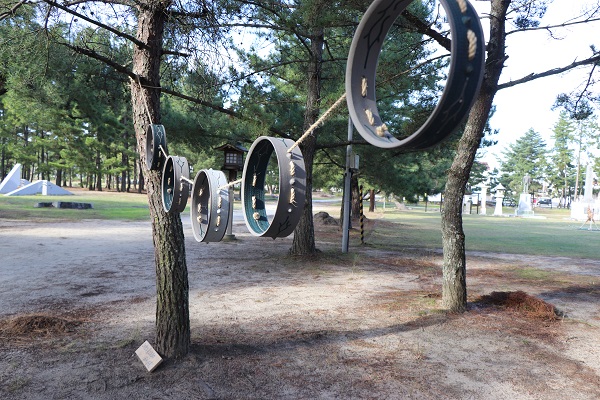 松の木々のあいだに丸い輪の造形物を吊るしたアートの写真