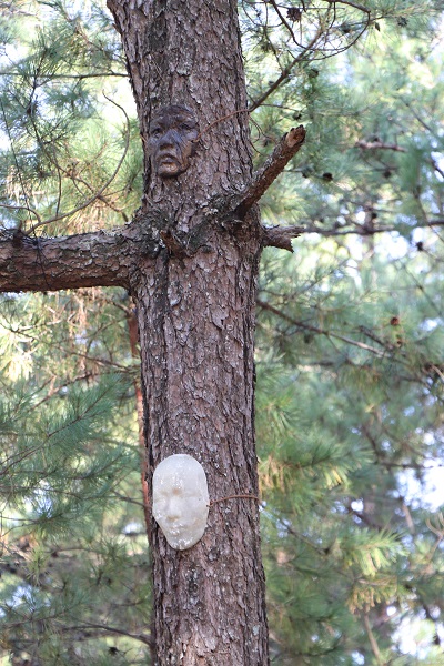 人の顔のようなお面が木につけられている造形アートの写真